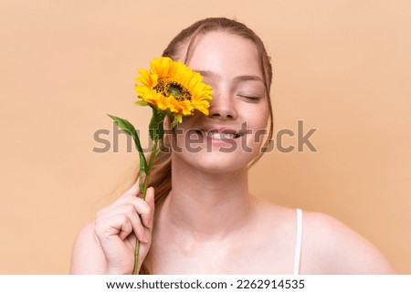 Young caucasian girl isolated on beige background holding a sunflower while smiling. Close up portrait Royalty-Free Stock Photo #2262914535