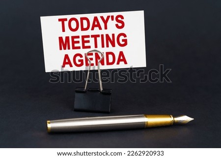 Business concept. On the black surface is a pen, an office paper clip with a business card on which is written - Today is meeting agenda
