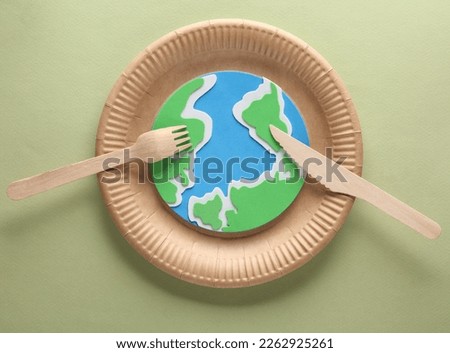 Planet earth on craft cardboard plate with wooden fork and knife on a green background. Plastic free, eco concept