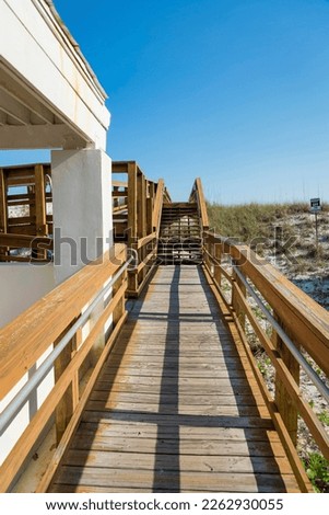 Wooden path with metal handrails at the side of the building near the white sand dunes- Destin, FL. Pathway heading to a stairs beside a building on the left and dunes on the right with keep out sign.