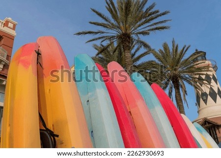 Lined standing colorful kayaks in low angle view at Destin, Florida. Kayaks against the views of palm trees and light house on the right under the blue sky background. Royalty-Free Stock Photo #2262930693