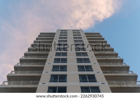 Low angle view of an apartment  hotel building in Destin, Florida under the giant clouds. Multi-storey building exterior with balconies on both corners and paned picture windows in the middle.