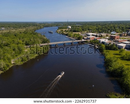 Wide river with passenger boat travelling under the bridges in Milton, Florida. River waterway in between the land areas with trees on left and buildings on the right connected by the bridges. Royalty-Free Stock Photo #2262931737