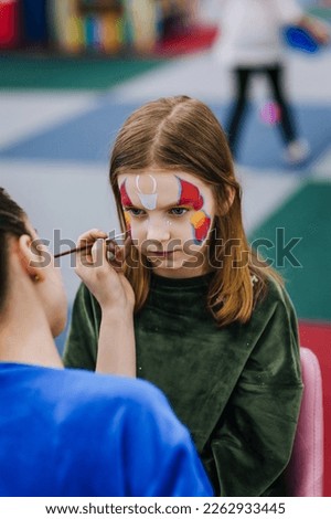 A professional make-up artist, artist paints with a brush on her face with face paints, drawing, children's makeup for a little girl model, a child. Photography, art, concept, lifestyle.