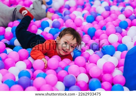 A beautiful, happy, small, smiling boy, a preschool child lies in a pile of multi-colored, colored plastic balls on the playground. Photography, portrait, concept.