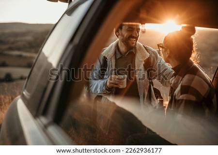 Young couple talking, drinking a coffee watching the sunset from their car. Couple travel concept Royalty-Free Stock Photo #2262936177