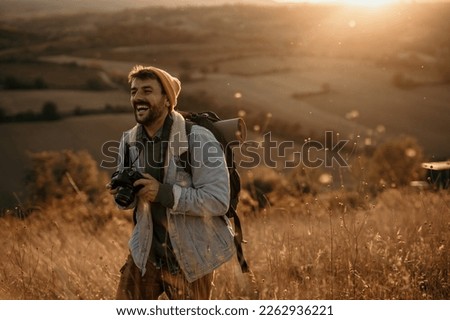 Smiling hiker tourist in the mountains at sunset. Man takes pictures of the sunset. Hipster with a photo camera and a backpack travels and enjoys nature. Copy space