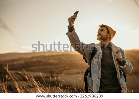 A male hiker standing on a hill trail, lifting his smartphone high in the air while looking for a signal. Copy space Royalty-Free Stock Photo #2262936239