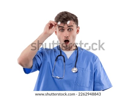 Doctor in uniform and with a stethoscope shows emotions of surprise and horror by opening his mouth and raising his glasses.