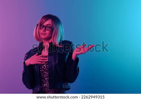 Shocked beautiful blonde woman in leather jacket sparkly dress trendy sunglasses look aside hold hand up posing isolated in blue pink color light background. Neon party Cyberpunk concept. Copy space