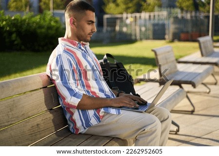 Handsome middle eastern programmer using laptop computer working freelance project online at workplace. Iranian student studying sitting on bench in university campus                             