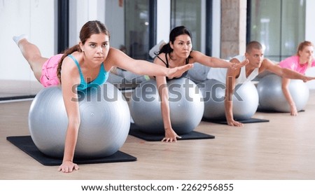 Adult sports people practiciting Pilates in the studio during a group training session perform an exercise on a fitness ball, ..which strengthens the lumbar region and develops overall flexibility Royalty-Free Stock Photo #2262956855