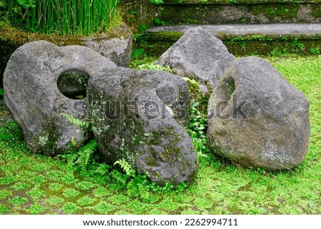 Group of four large gray boulders with holes sitting on checkered pattern of pavement and grass squares.