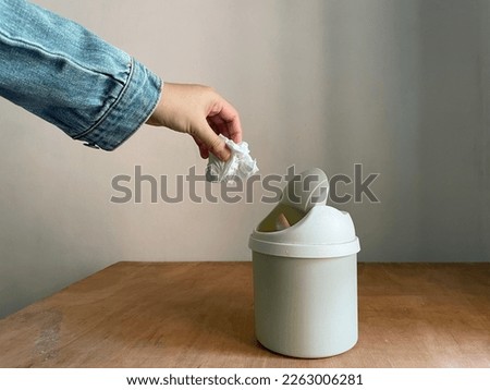 Female hand throwing away a crumpled tissue in small dustbin above wooden table Royalty-Free Stock Photo #2263006281