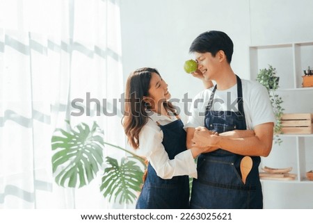Young Asian couple doing holiday together in the kitchen happily wearing apron. love and valentine concept