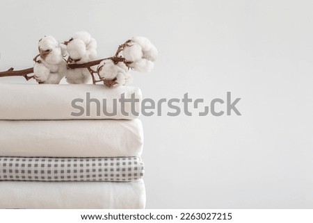 Cotton branch with pile of neatly folded bed sheets, blankets and towels. Production of natural textile fibers. Manufacture. Organic product. Royalty-Free Stock Photo #2263027215