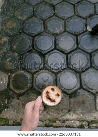 a cup of cappuccino coffee with a smile emoji shape on a paving background