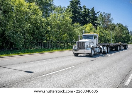 Industrial day cab classic big rig with oversize load sign on the roof transporting heavy cargo on flat bed semi trailers driving on the wide highway road with trees on the side in Columbia Gorge Royalty-Free Stock Photo #2263040635