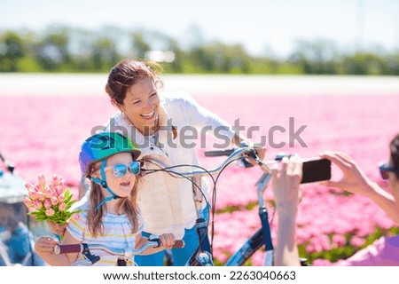 Dutch family riding bicycle in tulip flower fields in Netherlands. Mother and kids taking selfie picture with mobile phone camera on bikes at blooming tulips in Holland. Parents and children biking.
