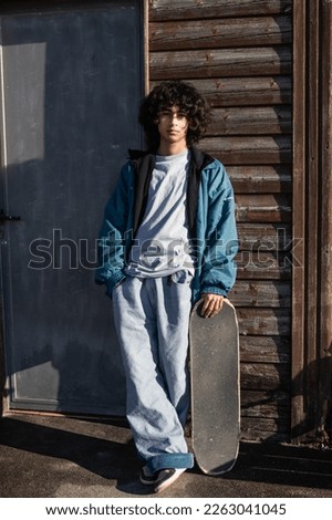 casual teenager with afro hair with skateboard on the wall