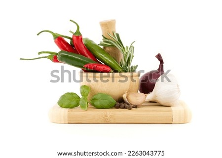 Chili peppers in wooden mortar, red onion, black pepper, basil sprig and garlic bulb isolated on white background. Spices, herbs and flavoring theme still life