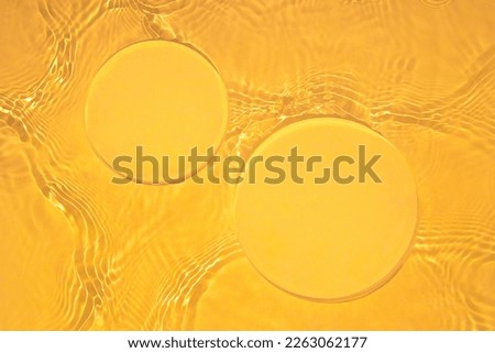 Two empty clear glass circle podiums on yellow transparent calm water texture with waves in sunlight. Abstract nature background for product presentation. Flat lay cosmetic mockup, copy space.