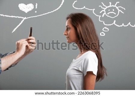 Male hands with a mobile phone take a picture of a beautiful young woman, but she thinks she is not at all - concept of self-esteem and self-efficacy in self-acceptance