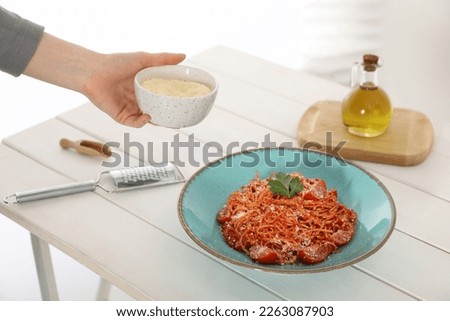 Food stylist holding grated cheese for spaghetti at white wooden table in studio, closeup