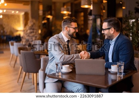 Two elegant stylish corporate leaders shaking hands after a successful business meeting in a restaurant in the evening. Proud business partners shaking hands while sitting at table in restaurant. Royalty-Free Stock Photo #2263091887