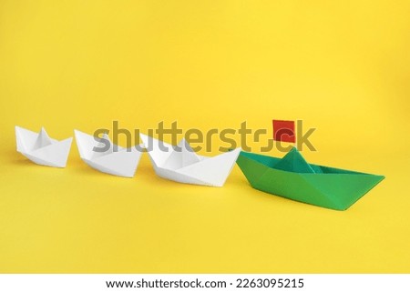 Group of paper boats following green one on yellow background,. Leadership concept
