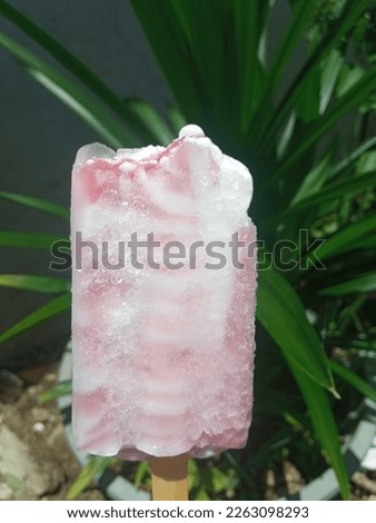 holding melted blueberry ice cream sticks in hands plant background during the day under the hot sun in Indonesia.

