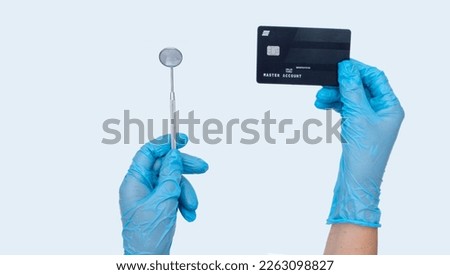 Female dentist hand holds dentist mirror and credit card. Light background. Concept of Cost of dental treatment