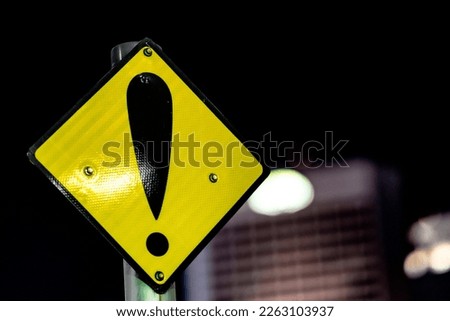Close-up view of a yellow warning traffic safety sign in the city with high rise building in the background