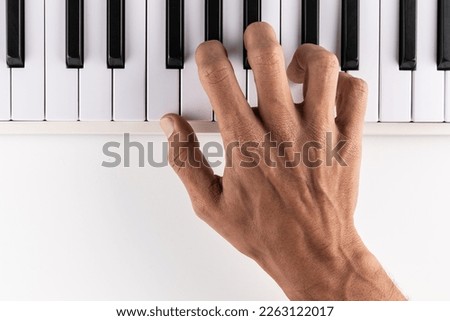Male hand playing piano, top view.