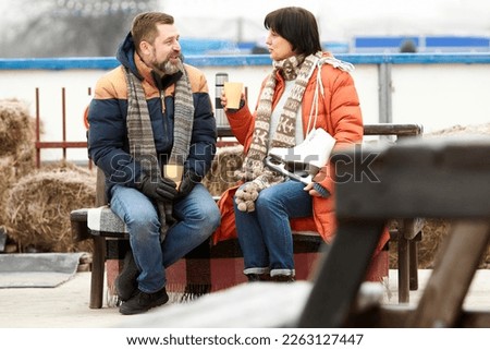 Mature man and woman visiting open air ice rink in winter. Warming up with hot drinks, tea, mulled wine. Cozy weekends. Concept of leisure activity, hobby, sport, vacation, fun, relationship, emotions