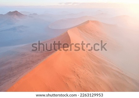 Orange dunes of the Namib Desert lit by sunrise: Aerial, panoramic photo of Sunrise over desertscape of the Namib. Namib-Naukluft National Park, Namibia