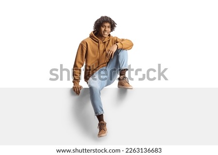 Young african american male sitting on a blank panel isolated on white background