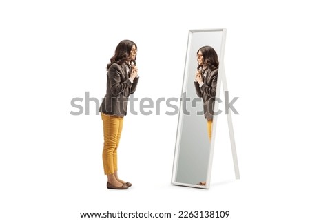 Full length profile shot of a young woman getting ready in front of a mirror and putting a scarf isolated on white background Royalty-Free Stock Photo #2263138109