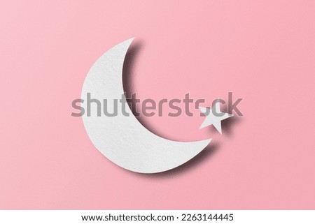 White paper cut into crescent shapes and stars set on pink paper background.
