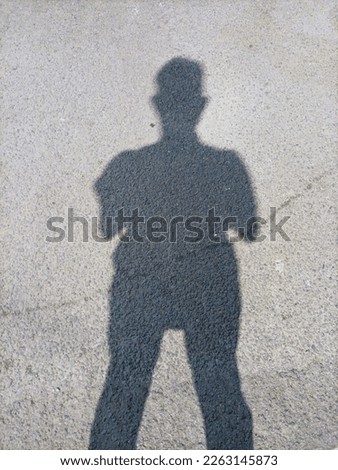 Shadowy silhouette of a man standing on asphalt background texture. Royalty-Free Stock Photo #2263145873