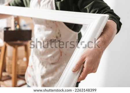 Cropped view of blurred restorer in apron holding wooden picture frame