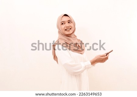Happy young asian muslim woman looking back while holding a cell phone. Isolated on white background