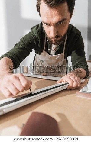 Bearded restorer in apron working with picture frame in workshop