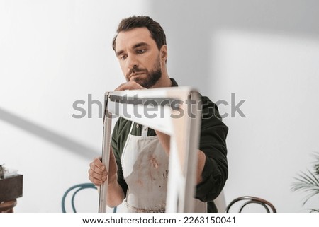 Bearded carpenter in workshop looking at picture frame in workshop