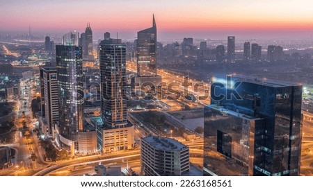 Aerial view of media city and al barsha heights district area night to day transition timelapse from Dubai marina. Towers and skyscrapers with traffic on a highway from above
