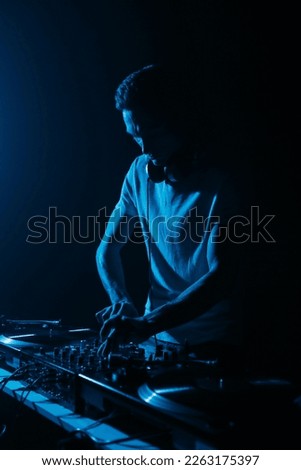 Silhouette of club DJ playing music on techno party. Disc jockey mixing musical tracks with sound mixer and vinyl records in blue light Royalty-Free Stock Photo #2263175397