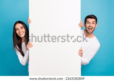 Portrait of two impressed positive people peek behind empty space blank isolated on blue color background Royalty-Free Stock Photo #2263182849