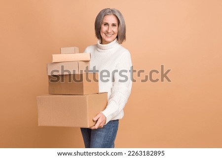 Photo of positive sweet lady dressed white sweater delivering boxes pile empty space isolated beige color background