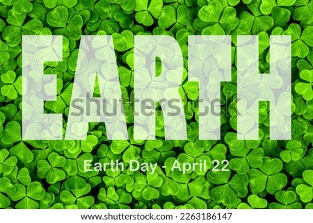 Lettering Earth Day April 22 on the background of clover leaves. Earth day concept, protection of the planet from pollution, improvement of environmental ecology and nature conservation.