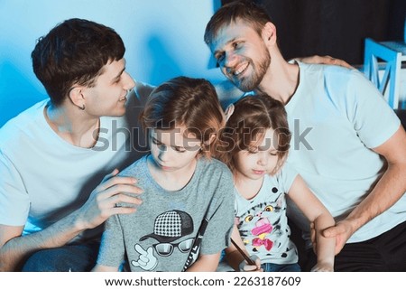   Staged photo. Homosexual couple and their children, two girls, at home.  A sweet smile for the partner. If parents take the time to be gentle with each other, children are happy in such a family.   